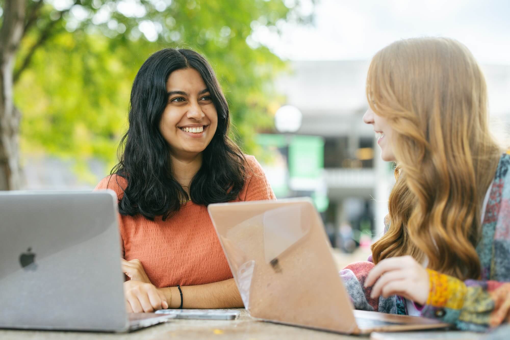 two students sitting outside the Memorial Student Center talking and working on laptops