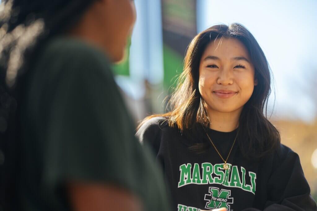 two students talking on campus and one smiling at the camera