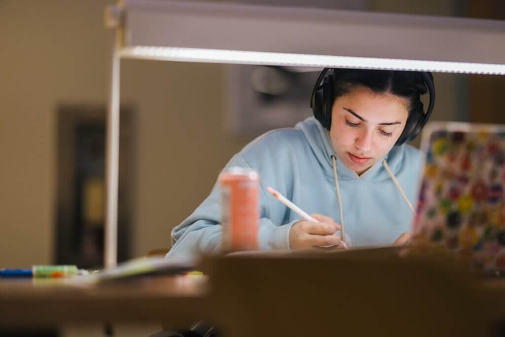 student working in the library on a laptop and also writing