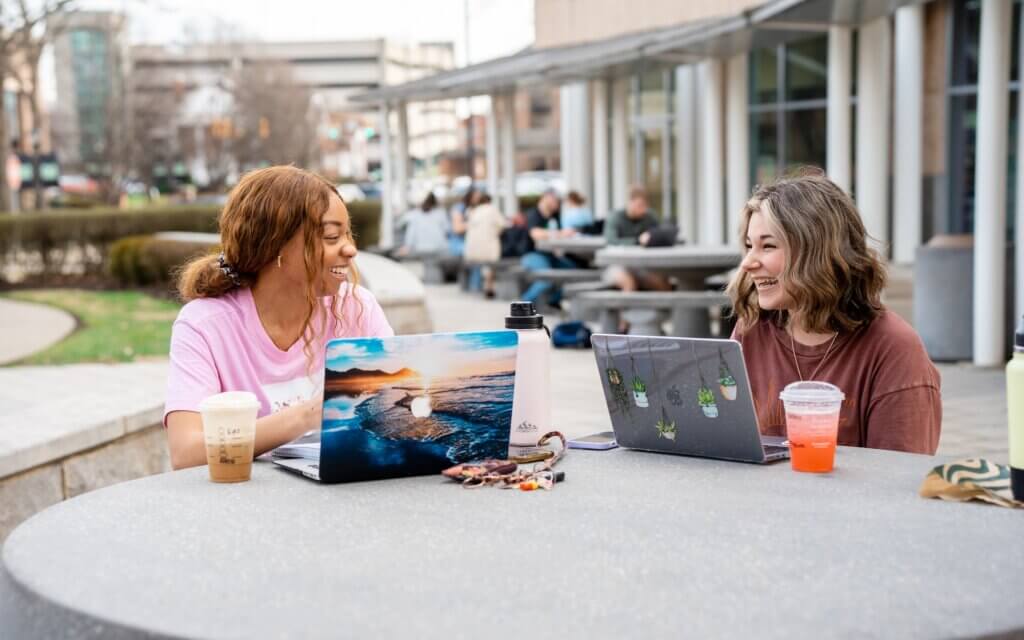 two students outside the library working on laptops