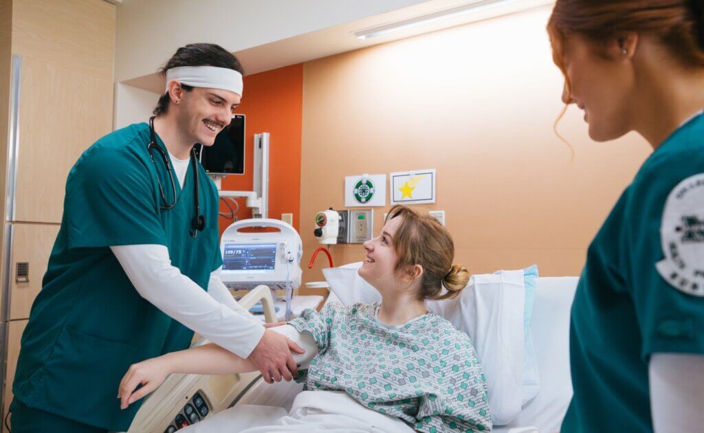 two nursing students working with a patient in a hospital bed