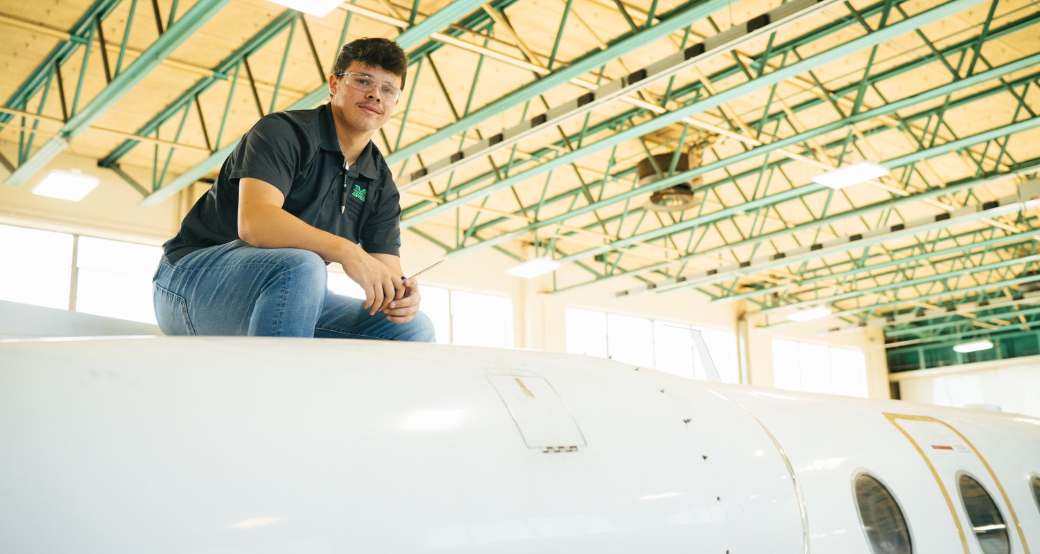 Marshall University Aviation Maintenance Technology student looks at the camera fron atop an aircraft.