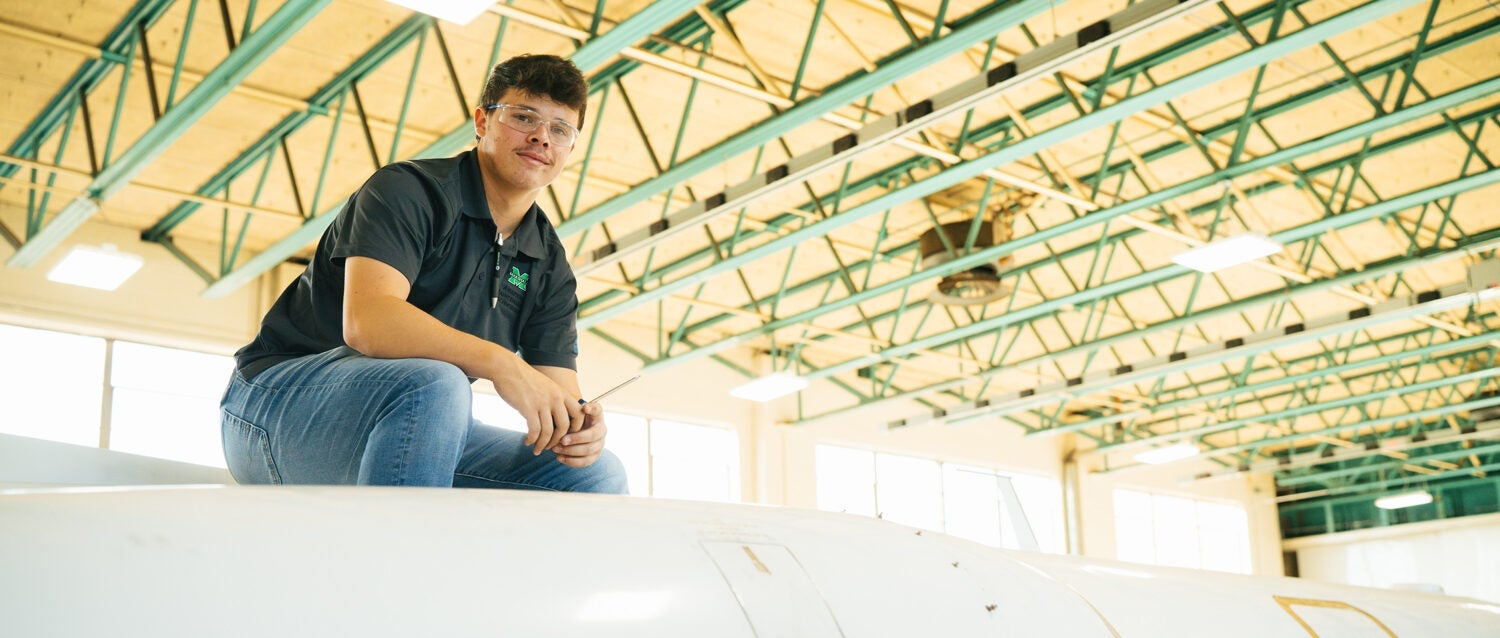 Marshall University Aviation Maintenance Technology student looks at the camera fron atop an aircraft.