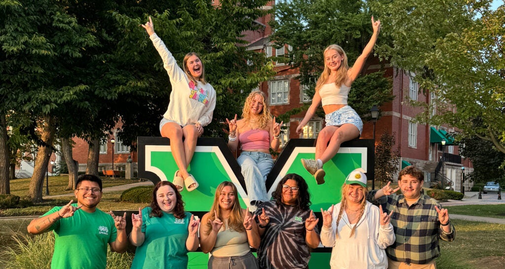 Marshall University Social Media Ambassadors smile together at a large Block M sign on Marshall's Huntington campus