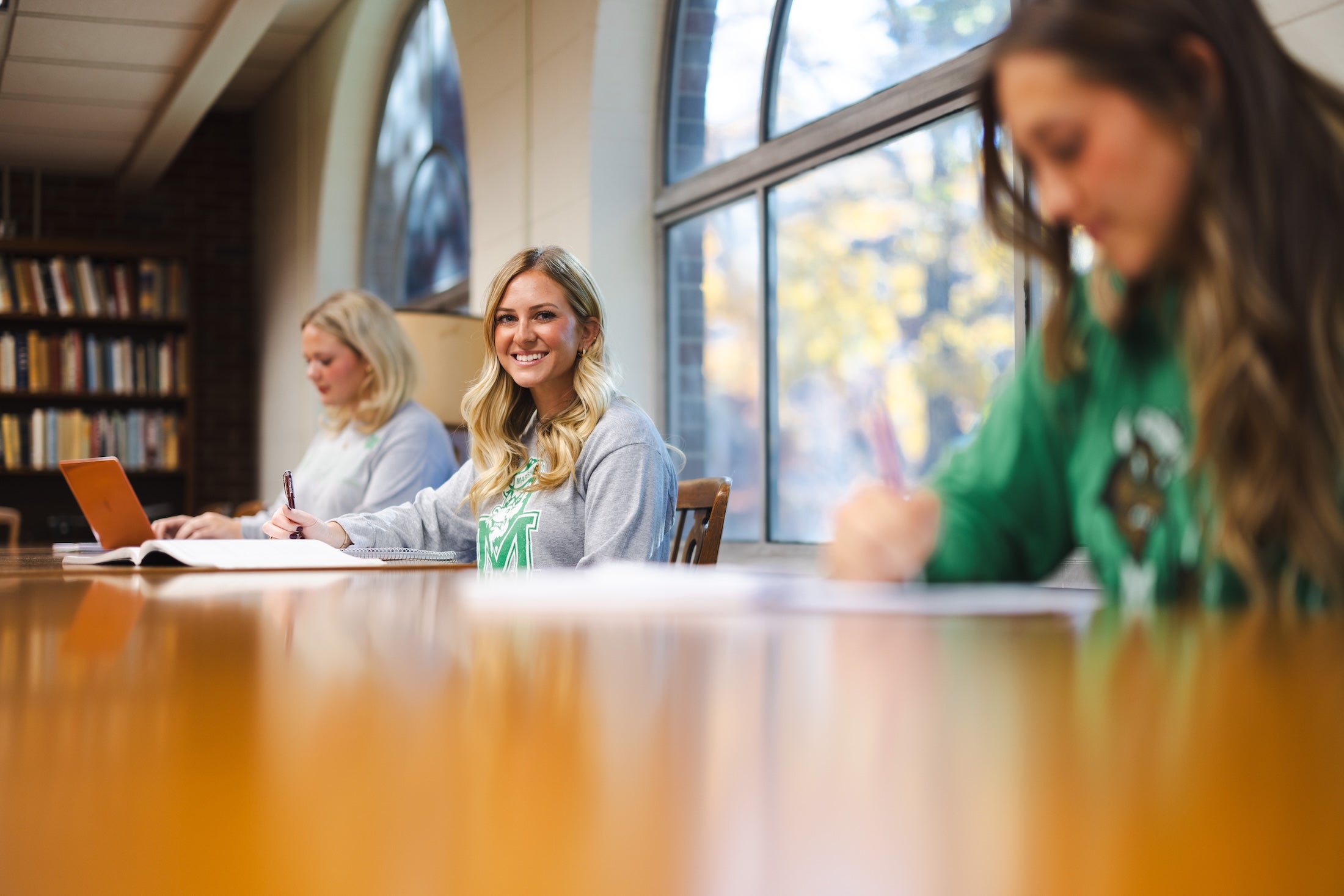 three students working in the library with one looking at the camera and smiling