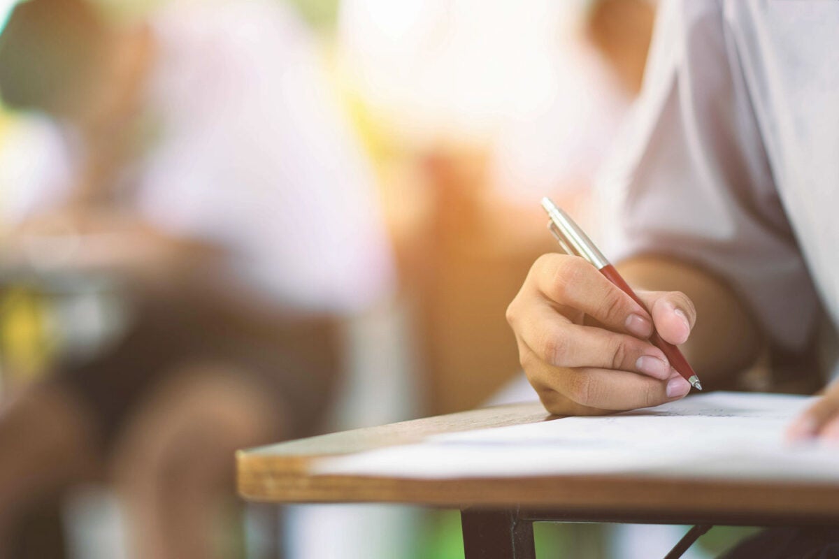 Closeup to hand of student holding pen and taking exam in classroom with stress for education test .