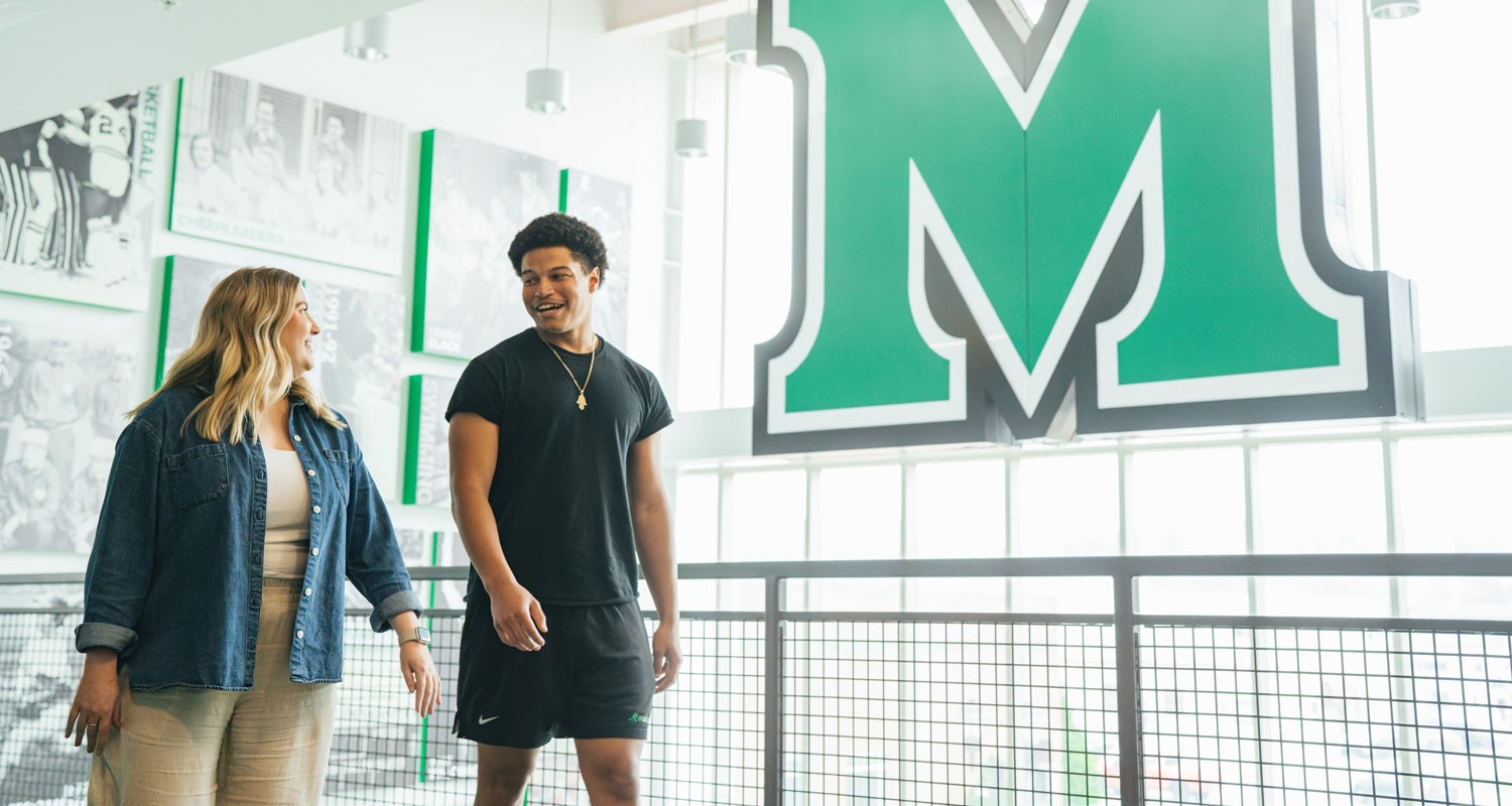 A student athlete and HELP advisor walk together through the Buck Harless Center at Marshall University