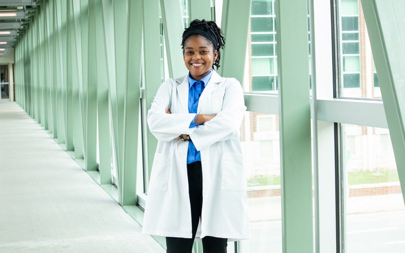 Marshall University Medical HELP student, wearing a white coat, stands on a campus sky bridge