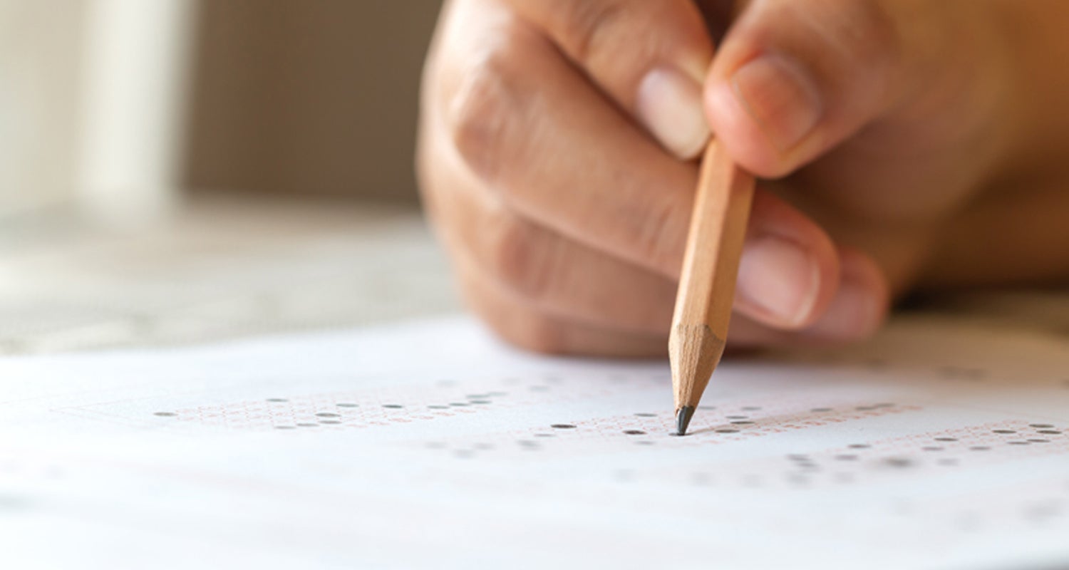 Hand holding a pencil filling in circles on a testing sheet