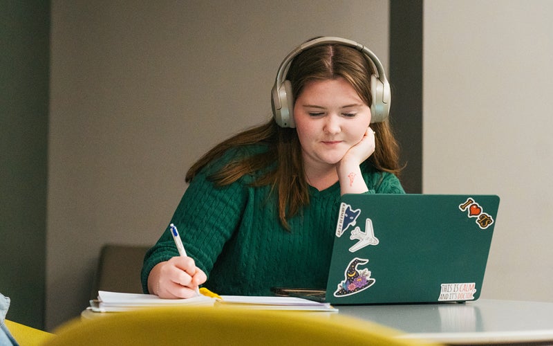 A student takes notes while watching a lecture on a laptop