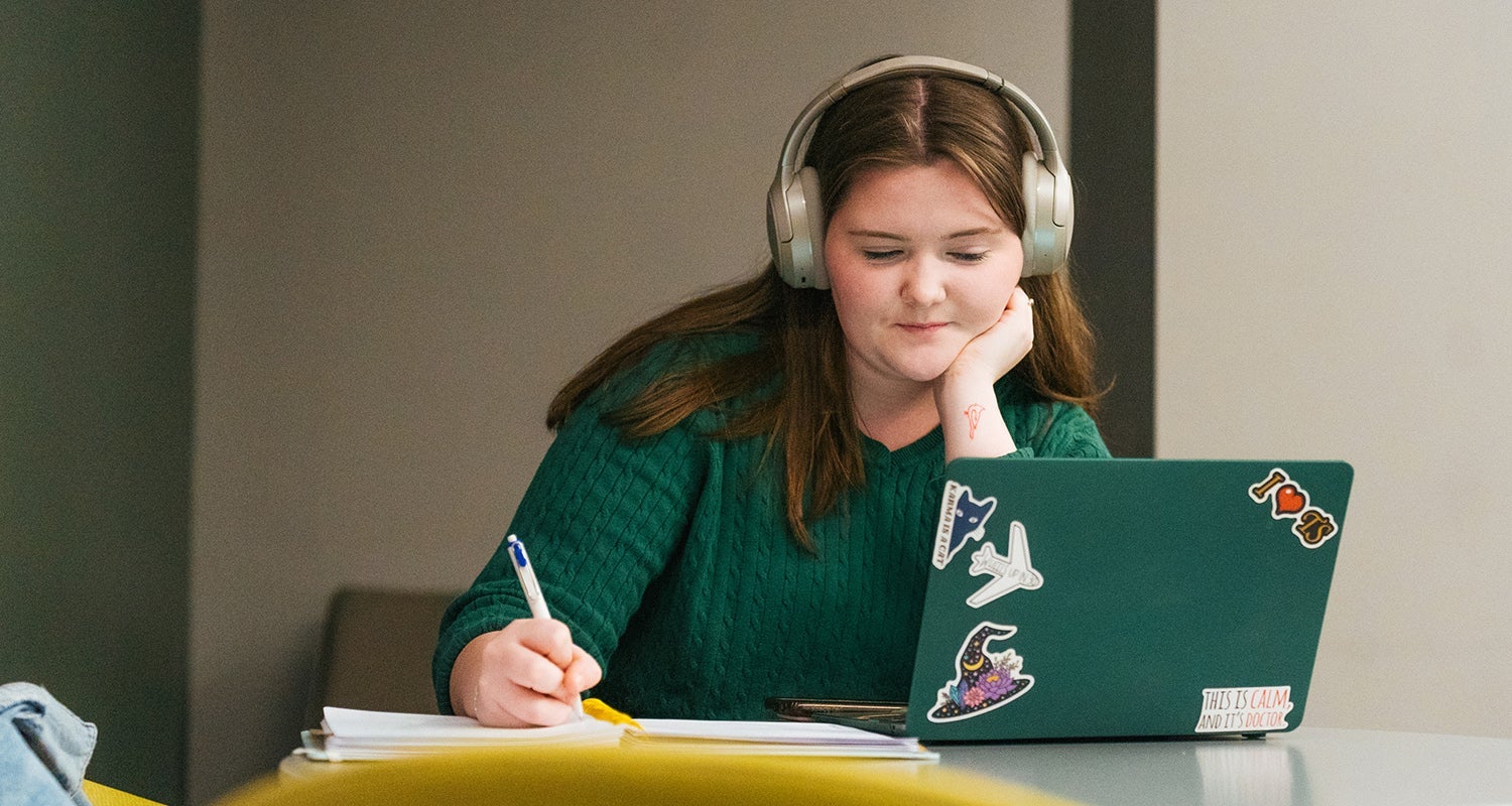 A student takes notes while watching a lecture on a laptop