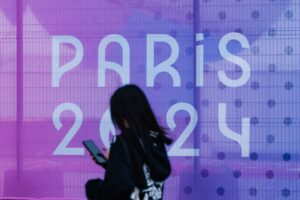 sign of Paris 2024 and a woman in front of it on her phone