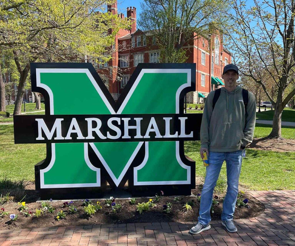 Jeremy Bailey stands by a large Marshall sign on Marshall University's Huntington campus