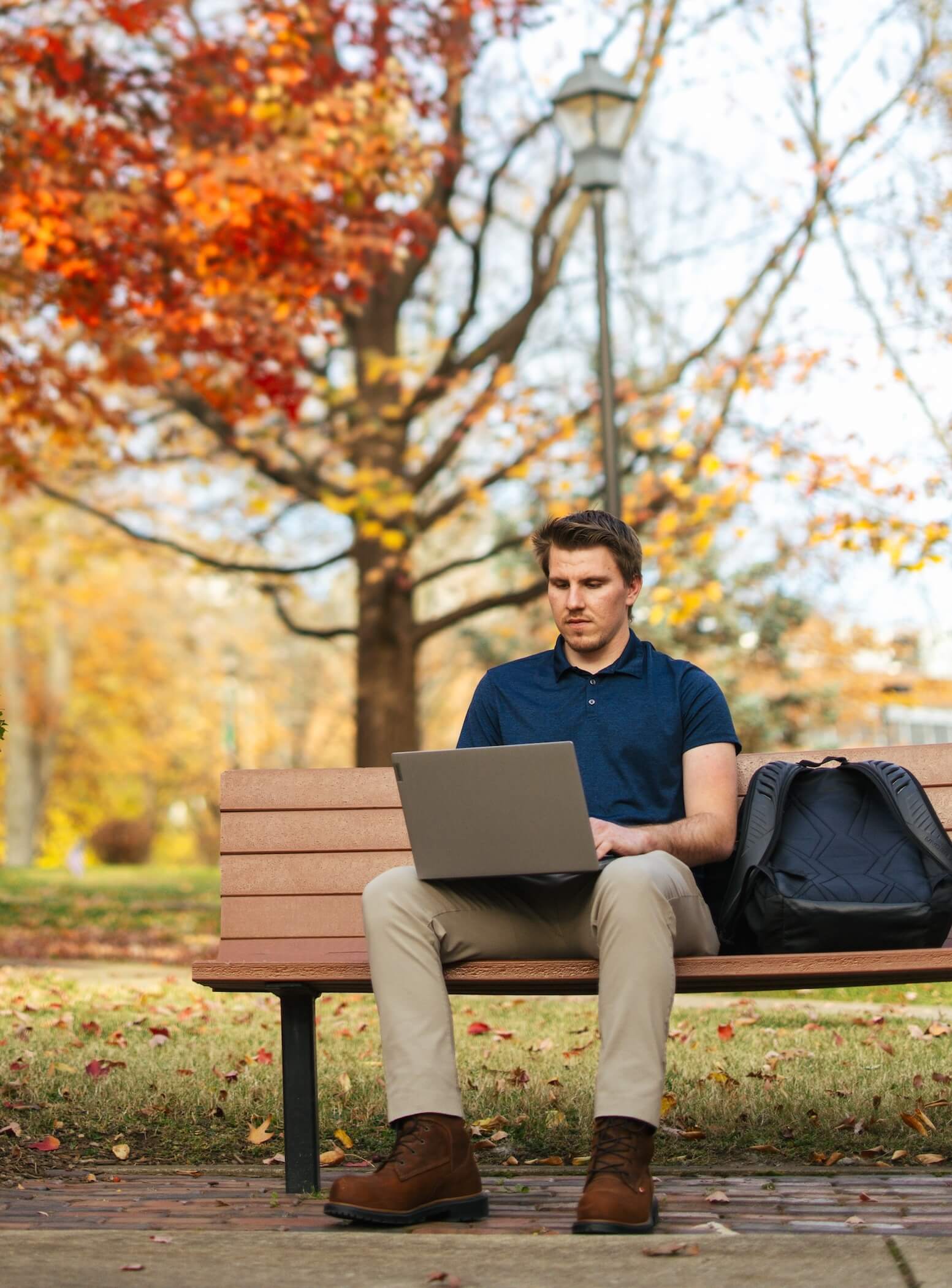 male student working on a laptop on a bench outside