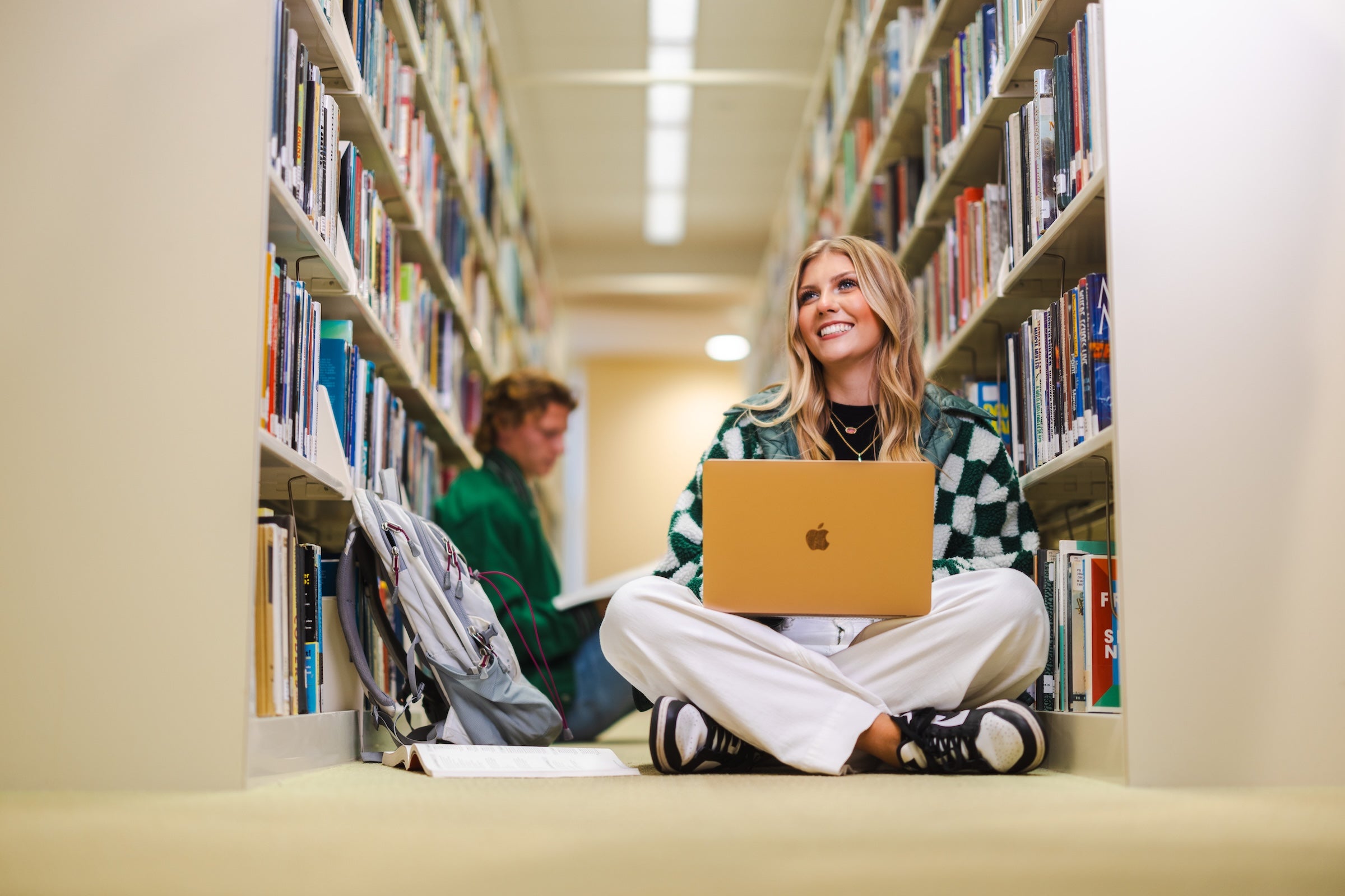 student working on a laptop in the library in between shelves