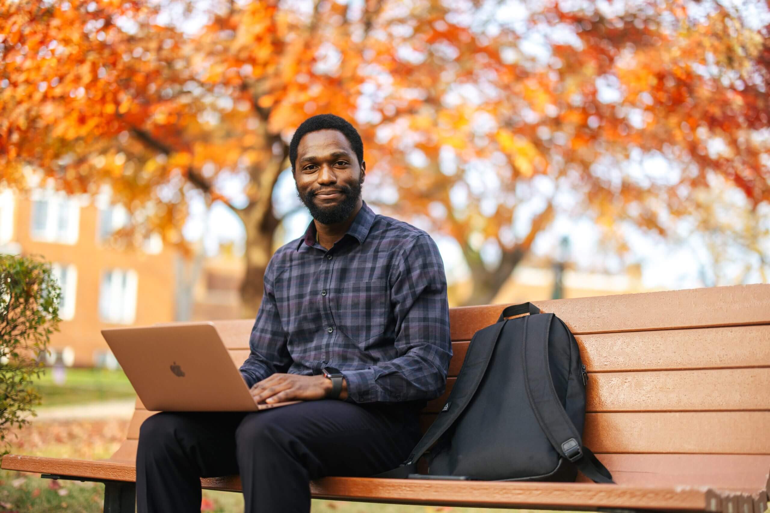 student using a laptop on a bench outside during fall