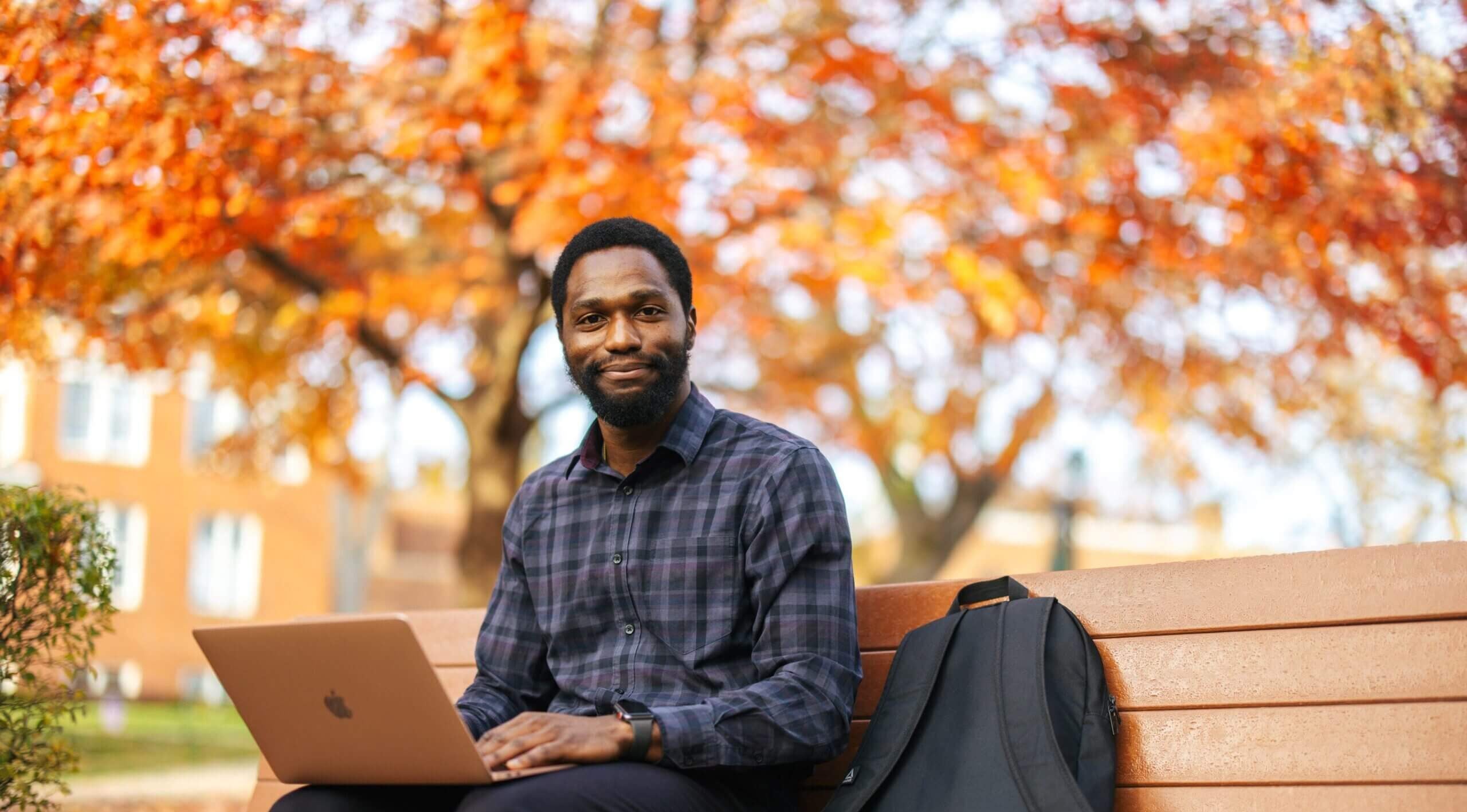 student sitting on a bench outside on a laptop