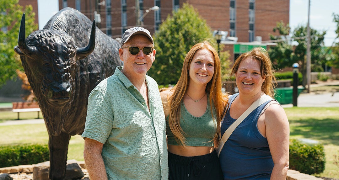 A student smiles with her family in front of a bison statue at Marshall University