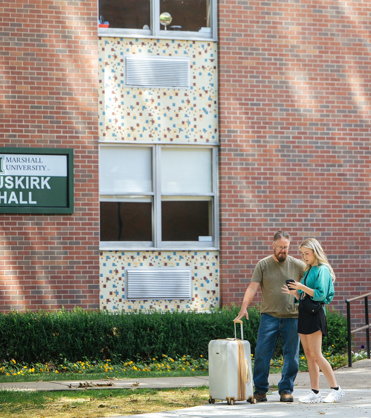 A father leans on a suitcase as his daughter shows him something on her phone during student move-in at Marshall University.
