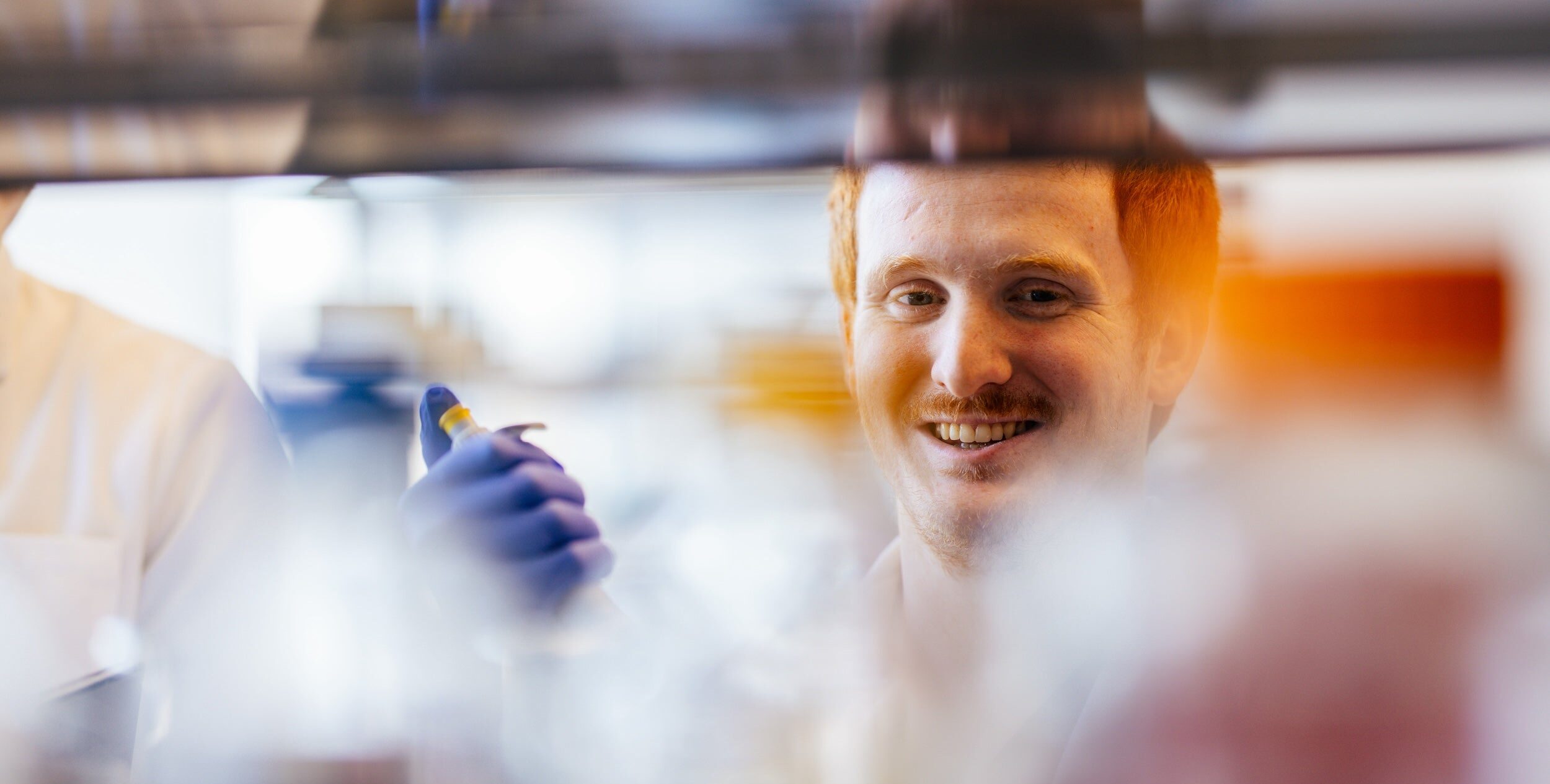 male pharmacy student working in a lab and smiling at the camera
