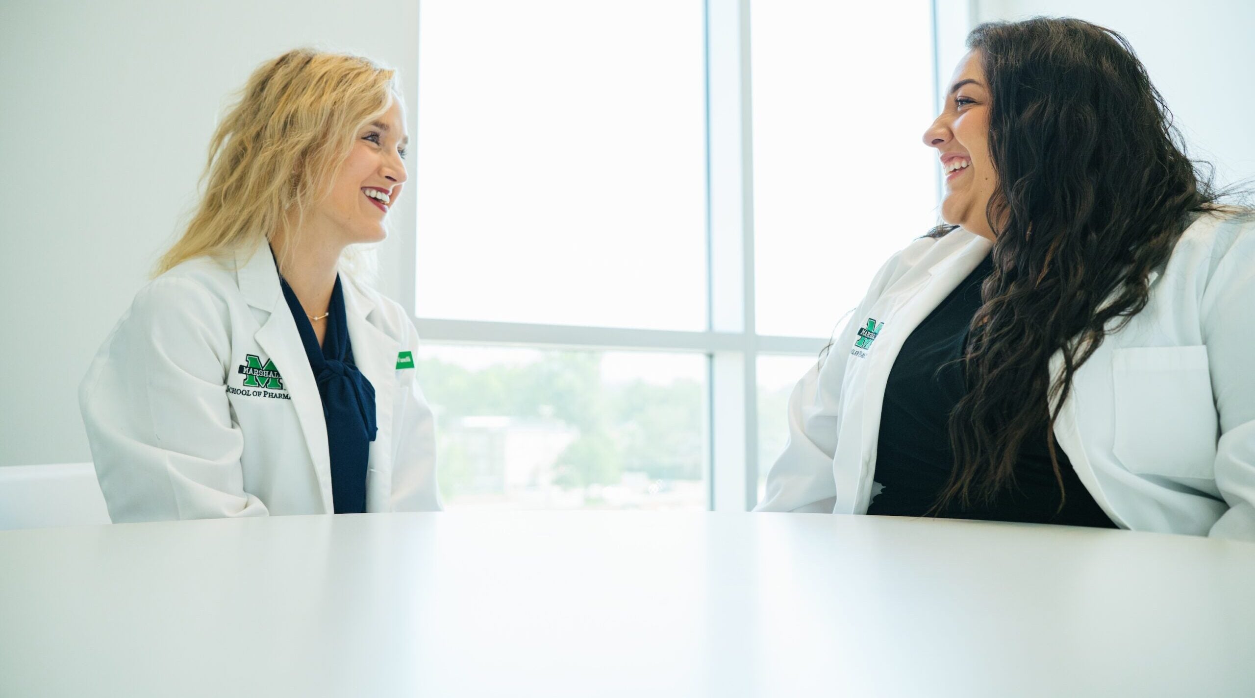 two pharmacy students talking to each other at a table