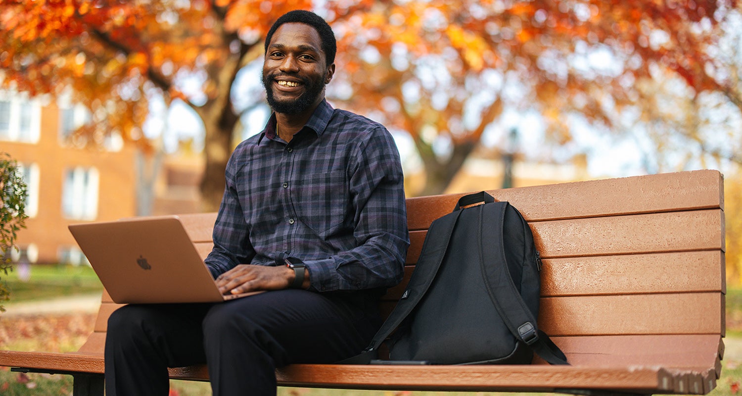 Student with a laptop, on a bench surrounded by fall colors