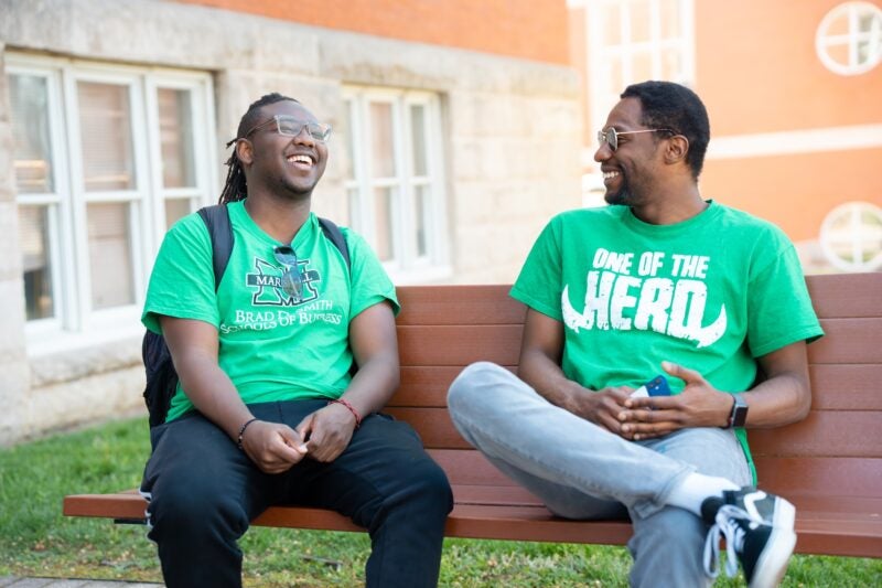 two students laughing on a bench outside