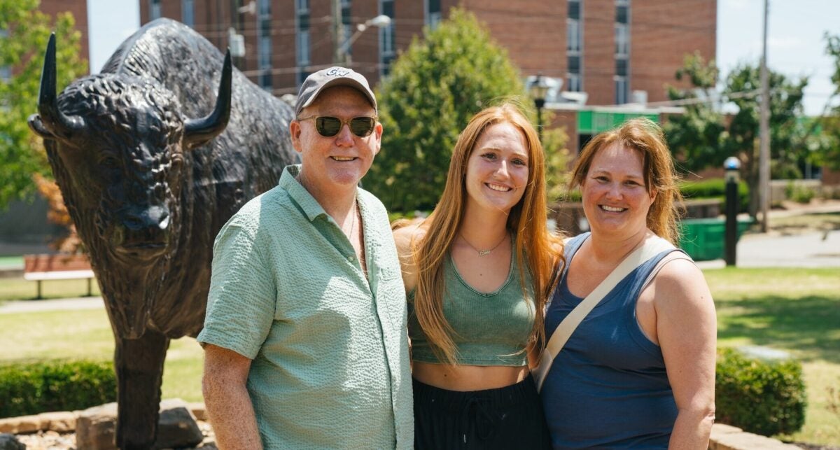 a dad, student and mom in front of the bison statue on campus