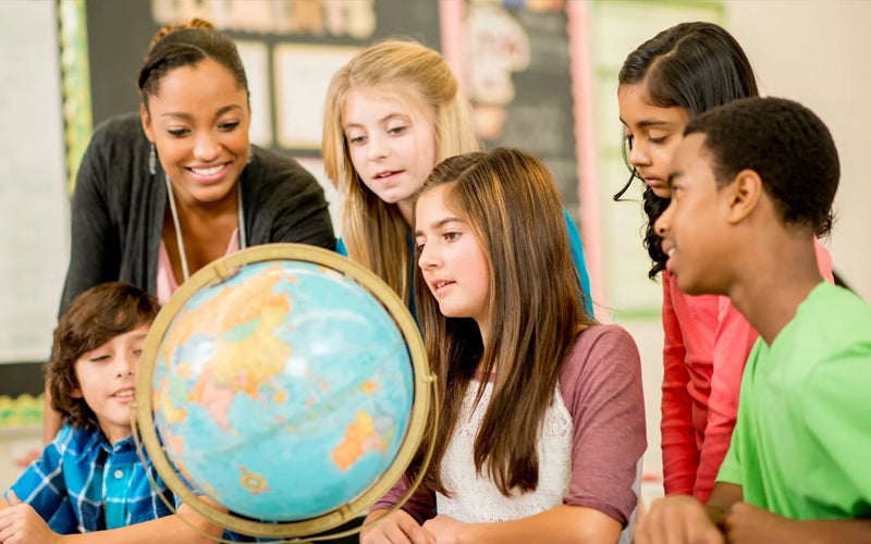 Teacher shows young students a location on a globe