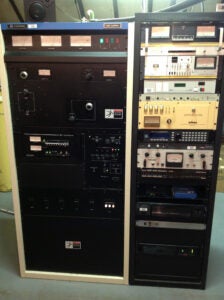 A Harris HT 3.5K FM transmitter is on the left. A rack full of other radio equipment is to the right.